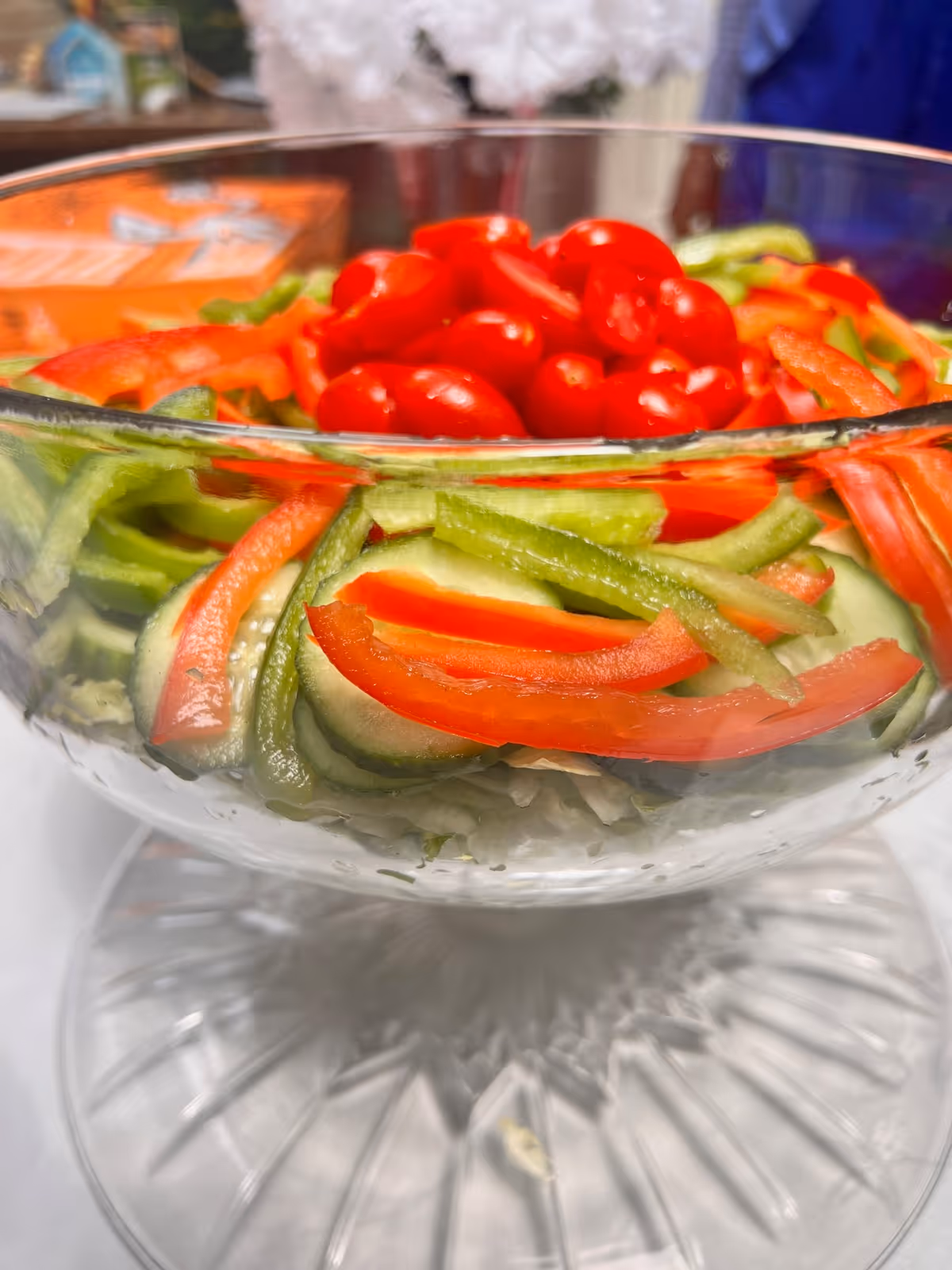 Glass bowl of salad with sliced cucumbers, red and green bell peppers and cherry tomatoes.