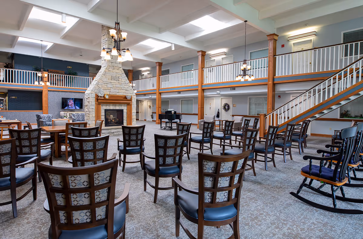 Spacious two-story assisted living common area with rows of chairs facing a central stone fireplace and balcony-level corridors.