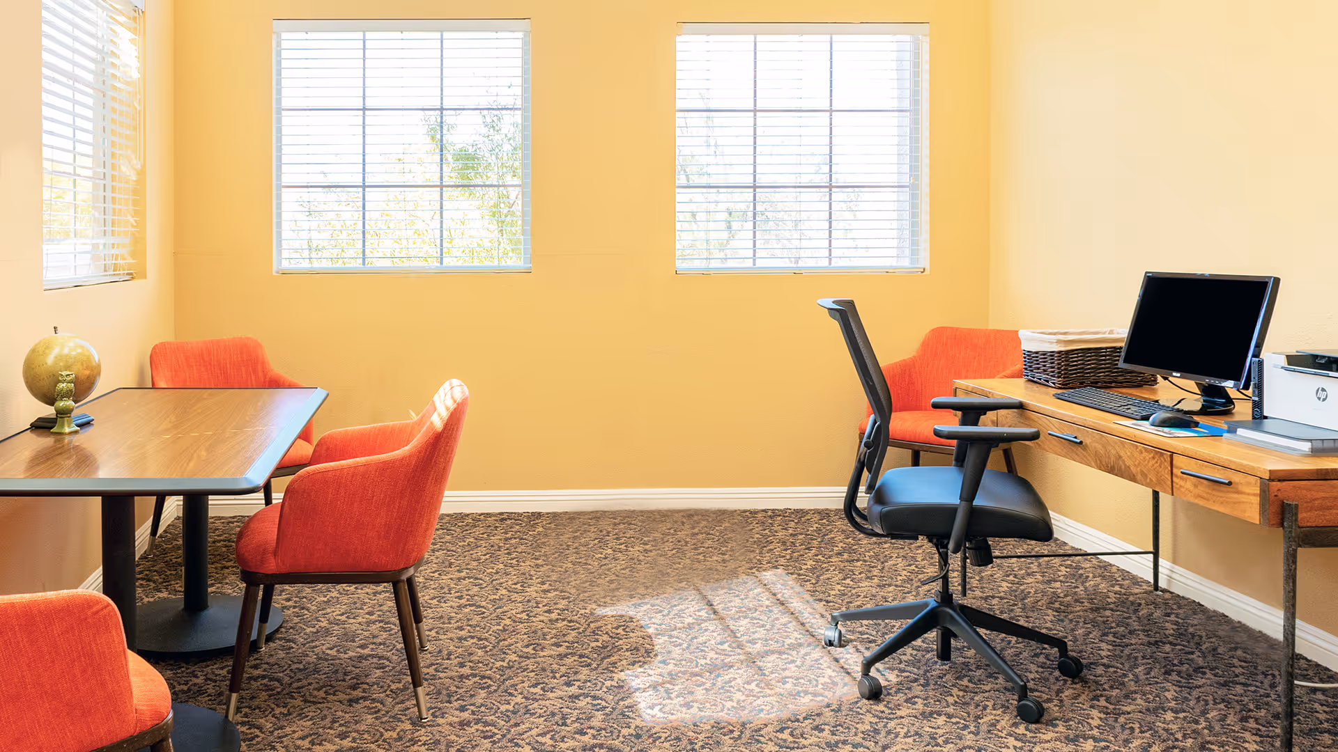 Bright small office room with two windows, orange chairs, a desk with a computer and printer.