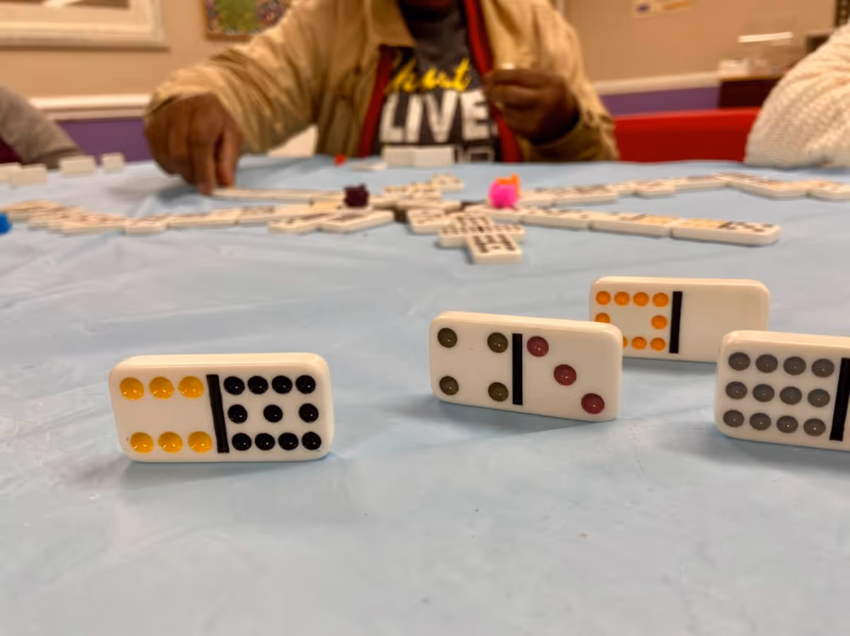 Close-up view of domino tiles standing on a blue tablecloth with a person in the background playing the game at Willow Ridge Memory Care.