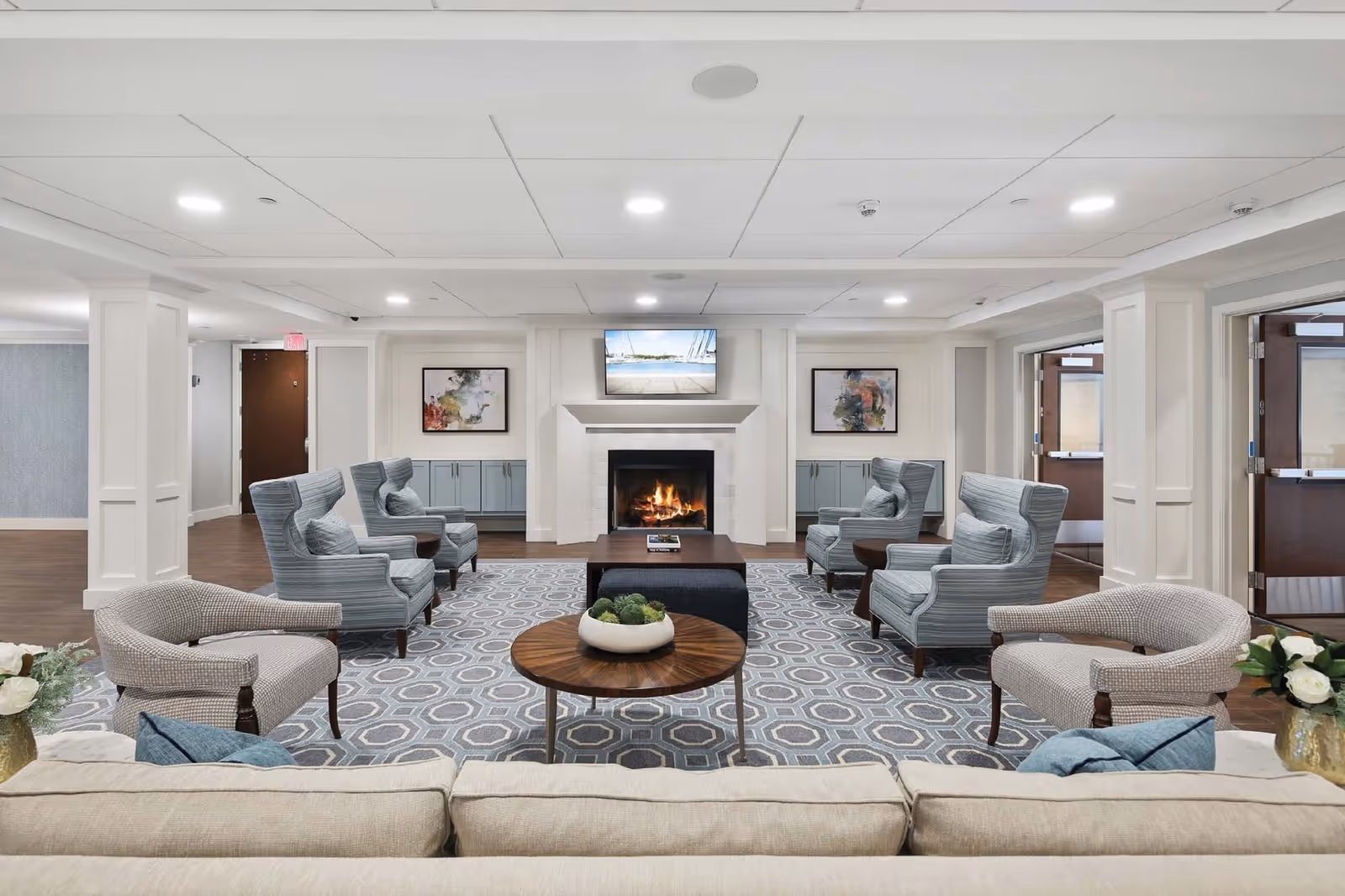 Spacious communal sitting area with a fireplace, TV, and arranged armchairs and sofas around a coffee table.