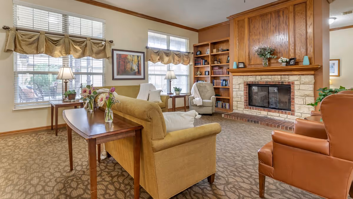 Cozy living room with sofas and armchairs arranged around a stone fireplace and built-in bookshelves beneath large windows.