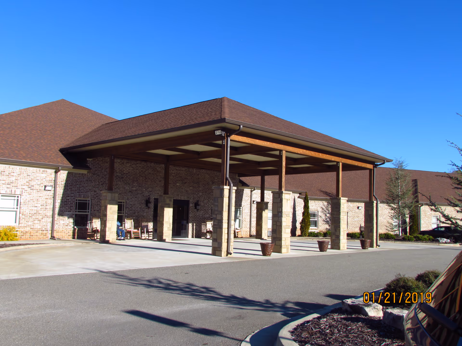 Covered entrance and porte-cochère of a brick assisted living building with rocking chairs on the porch.