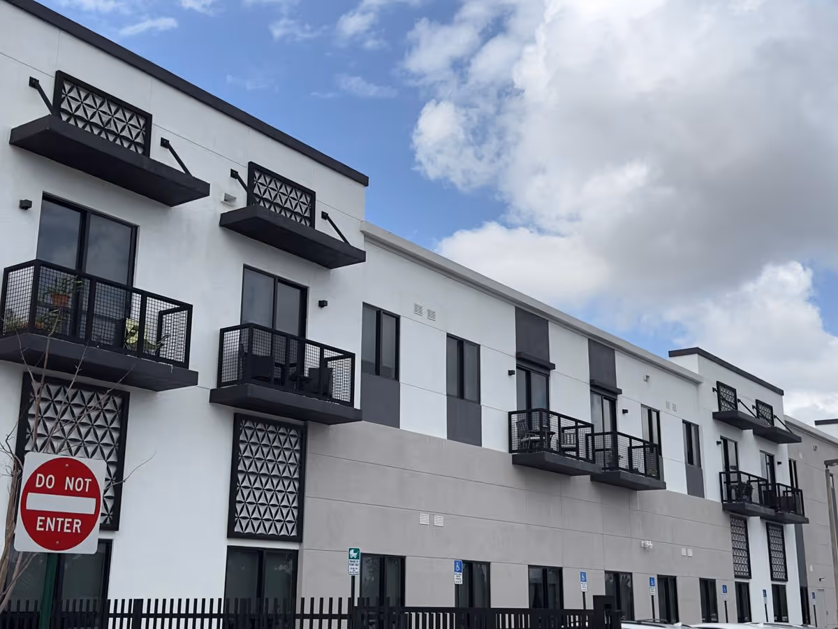 Street-level view of a modern three-story apartment building with small black balconies, decorative panels, and a 'Do Not Enter' sign in front.