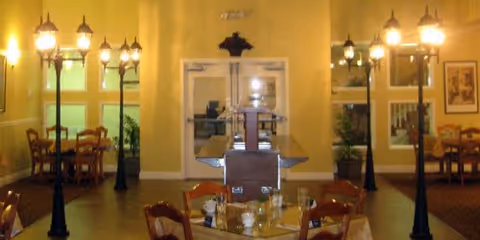 Interior dining room with wooden tables and chairs, decorative streetlamp-style floor lamps, and double doors centered on a warm yellow wall.