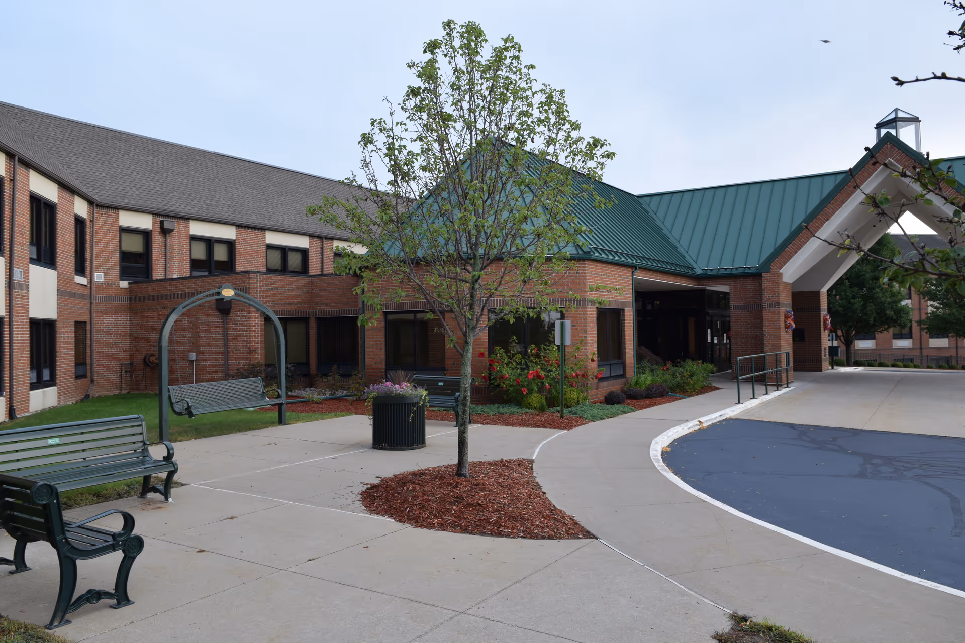 Front entrance of a brick senior living facility with a covered driveway, benches, and landscaping.