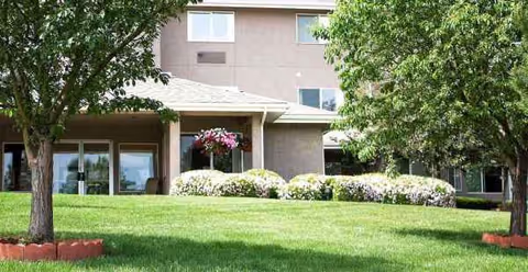 Exterior view of Quincy Place facility with green lawn, trees, and shrubs by entrance.