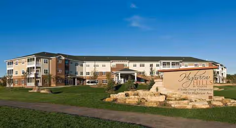 Exterior view of Highview Hills senior living facility with landscaped entrance and blue sky.