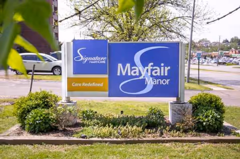 Exterior sign for Mayfair Manor with landscaping and a parking lot in background