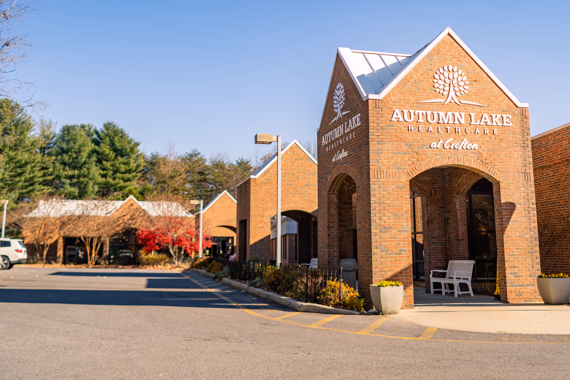 Brick front entrance of Autumn Lake Healthcare at Crofton with arched portico, signage, and adjacent parking area.