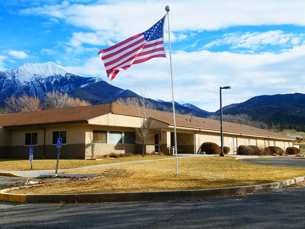 One-story facility building with an American flag on a flagpole and snow-capped mountains in the background.