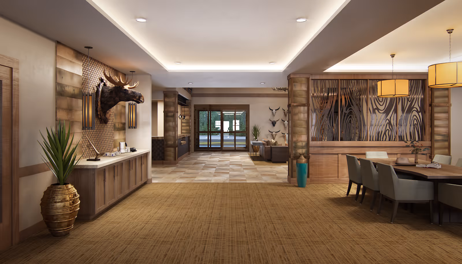 Spacious interior area of a senior living facility with a rustic design. On the left, there is a wooden cabinet with a mounted moose head above it and two hanging pendant lights. A large potted plant is placed beside the cabinet. The floor is carpeted in the foreground and transitions to tiled flooring toward the back. On the right, there is a dining area with a wooden table and several chairs, illuminated by two large pendant lights. The back wall features glass doors leading outside and a seating area with decorative animal skulls mounted on the wall.
