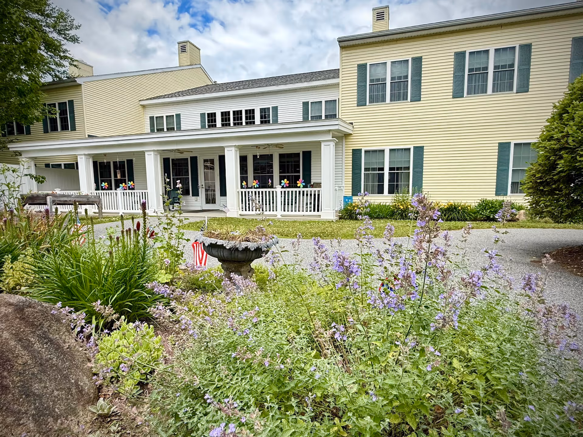 Yellow two-story building with a covered front porch and colorful flower beds in the foreground.