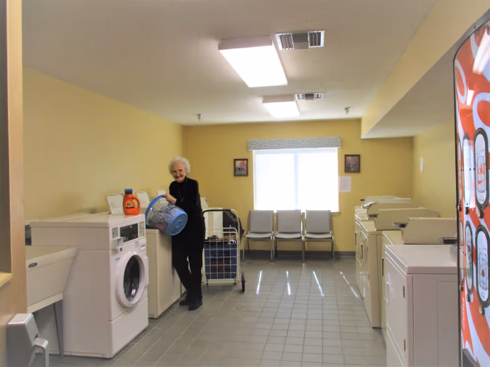 Elderly woman doing laundry in a communal senior-apartments laundry room.