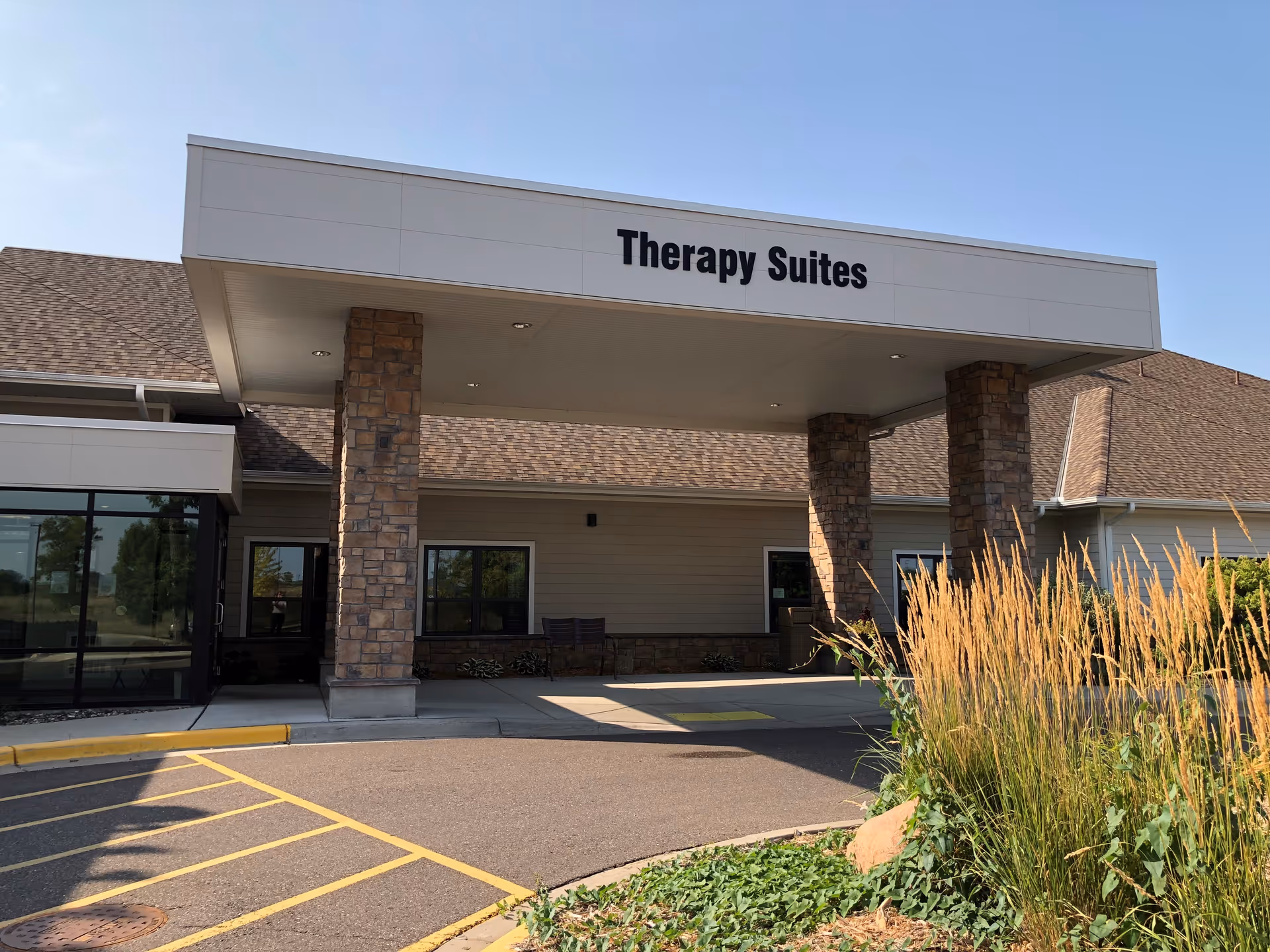 Front entrance of the Therapy Suites building showing a covered drive-through entrance with stone pillars and landscaping.