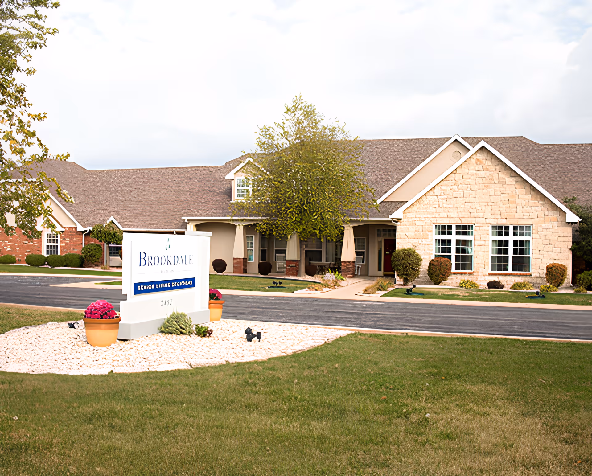 Front exterior of a single-story senior living building with a landscaped lawn and a Brookdale sign.
