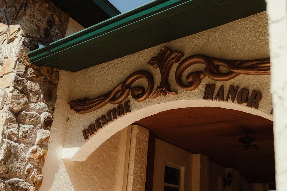 Close-up view of the entrance archway of Prestige Manor Assisted Living Facility Belleview, featuring decorative wooden carvings and stone wall accents.