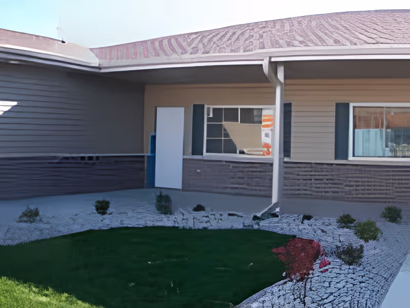 Front exterior of a single-story building with a covered walkway, windows, a door, and a small landscaped lawn.