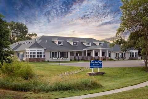 Prairie Senior Cottages exterior with lawn, walkway, and a blue sign in front.
