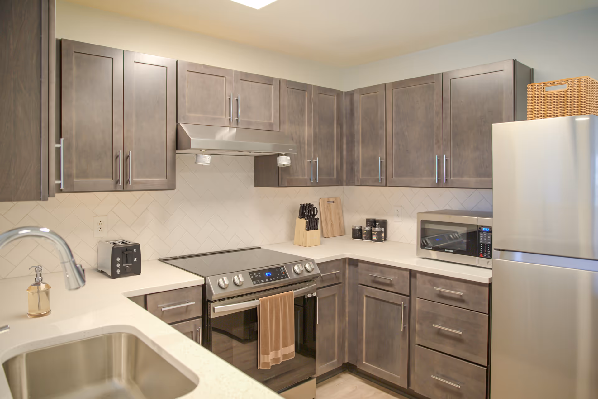 L-shaped kitchen with gray cabinets, stainless appliances, microwave, sink, and refrigerator.