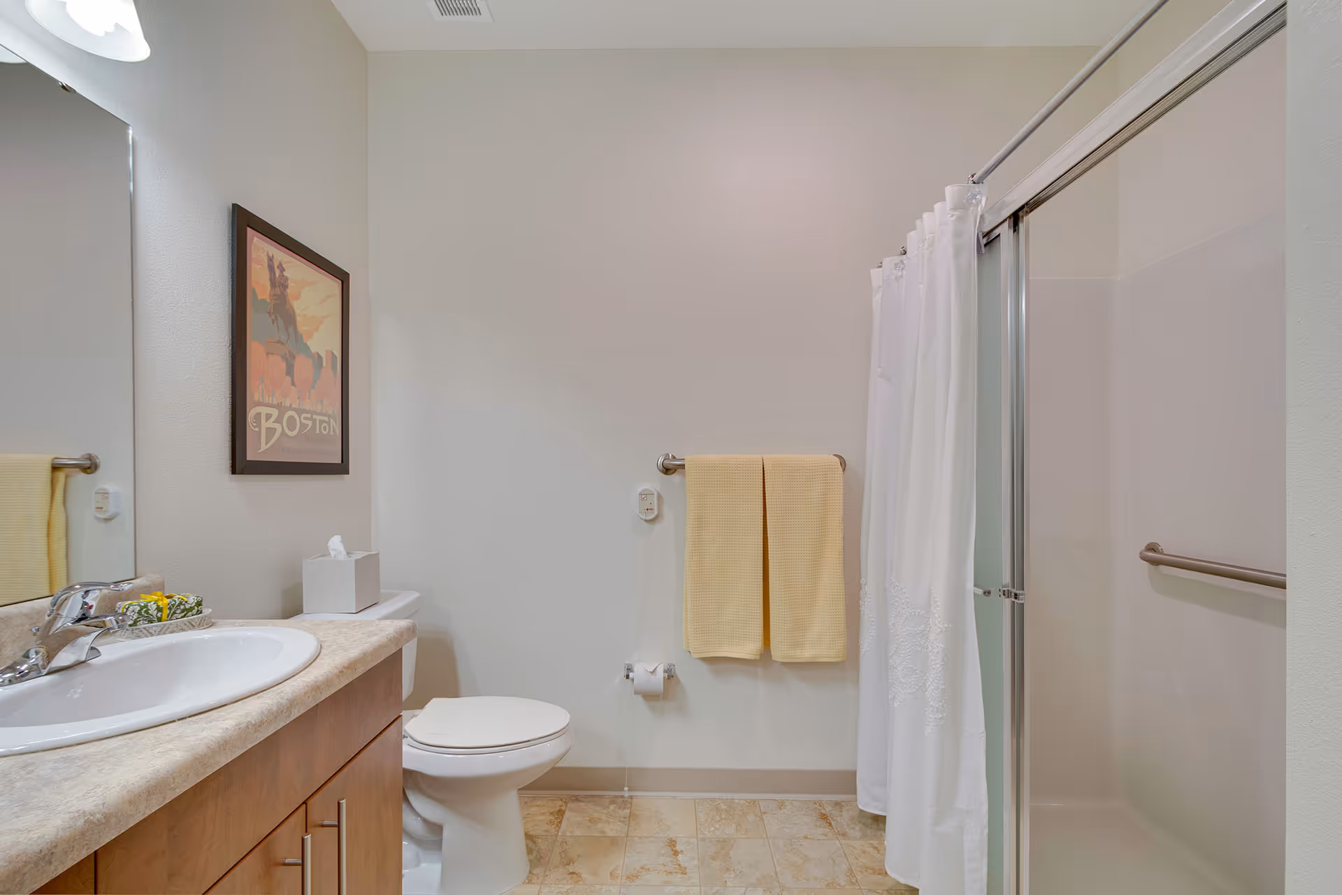 Bright bathroom with a sink and vanity, toilet, shower with curtain and grab bar, and yellow towels on a wall rack.