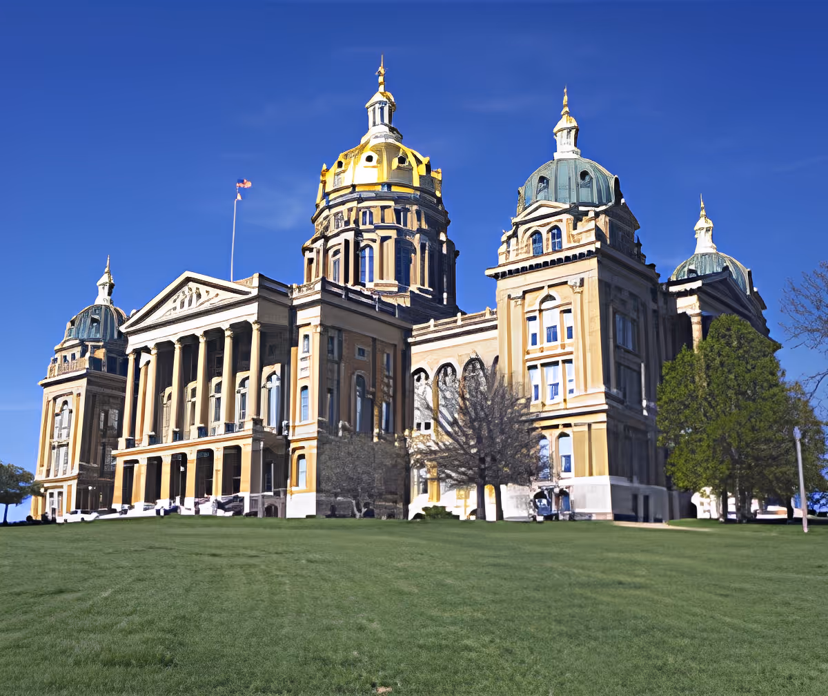 Large classical-style building with domes and columns standing on a grassy lawn under a clear blue sky.