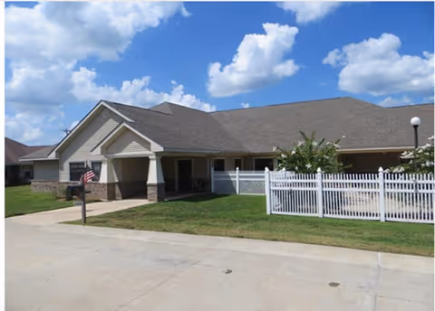 Single-story building with a covered entrance, white picket fence, mailbox with an American flag, and a blue sky.