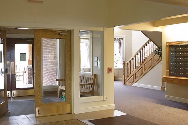 Interior lobby showing glass entry doors, a wooden bench, a staircase and a wall of mailboxes.