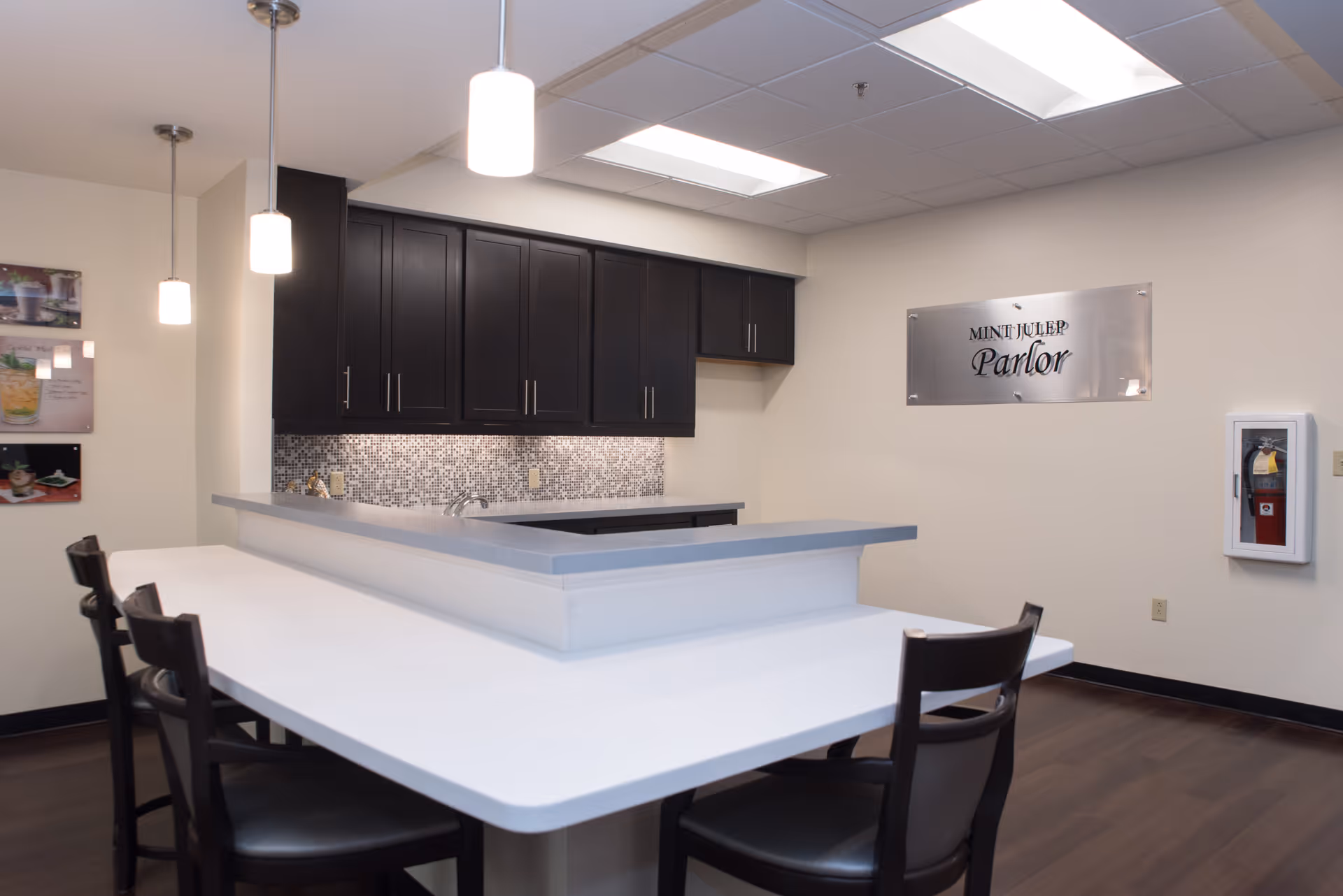 Communal kitchen and dining counter with bar stools, pendant lights, dark cabinets, and a "Mint Julep Parlor" sign on the wall.