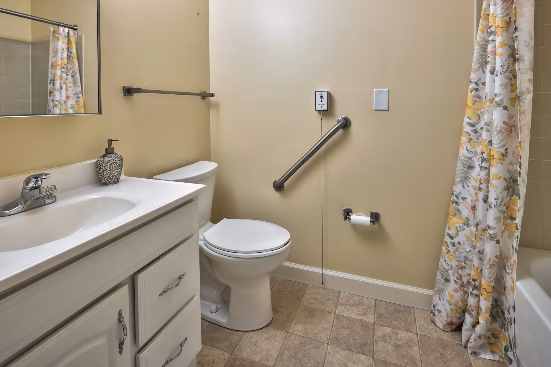 Small accessible bathroom with a sink and vanity, toilet with a grab bar, and a floral shower curtain.