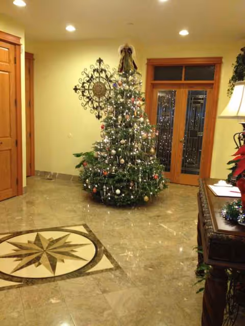 Bright senior living lobby with a decorated Christmas tree beside double wooden doors.