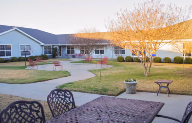 Outdoor courtyard with metal patio tables and chairs, winding concrete paths, lawn and a one-story building in the background.