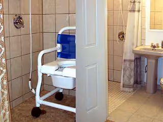 Blue and white shower chair in an accessible bathroom beside a sink with tiled walls.