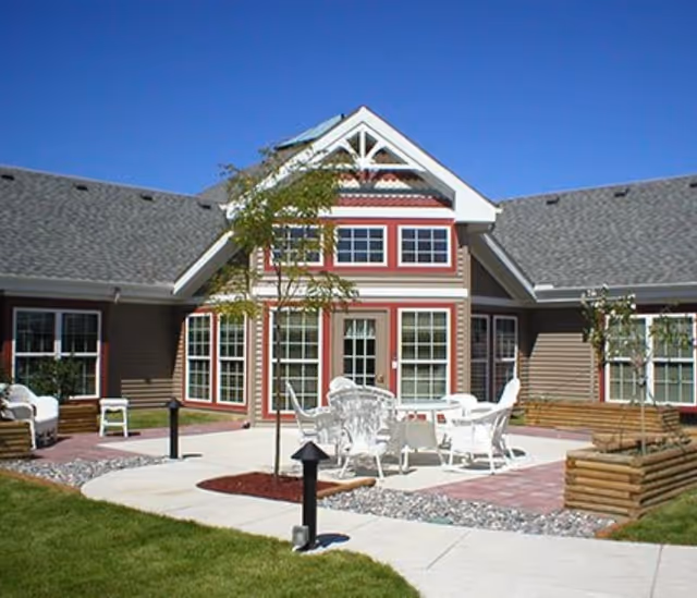 Exterior courtyard with white patio furniture in front of a multi-windowed senior living building under a clear blue sky.
