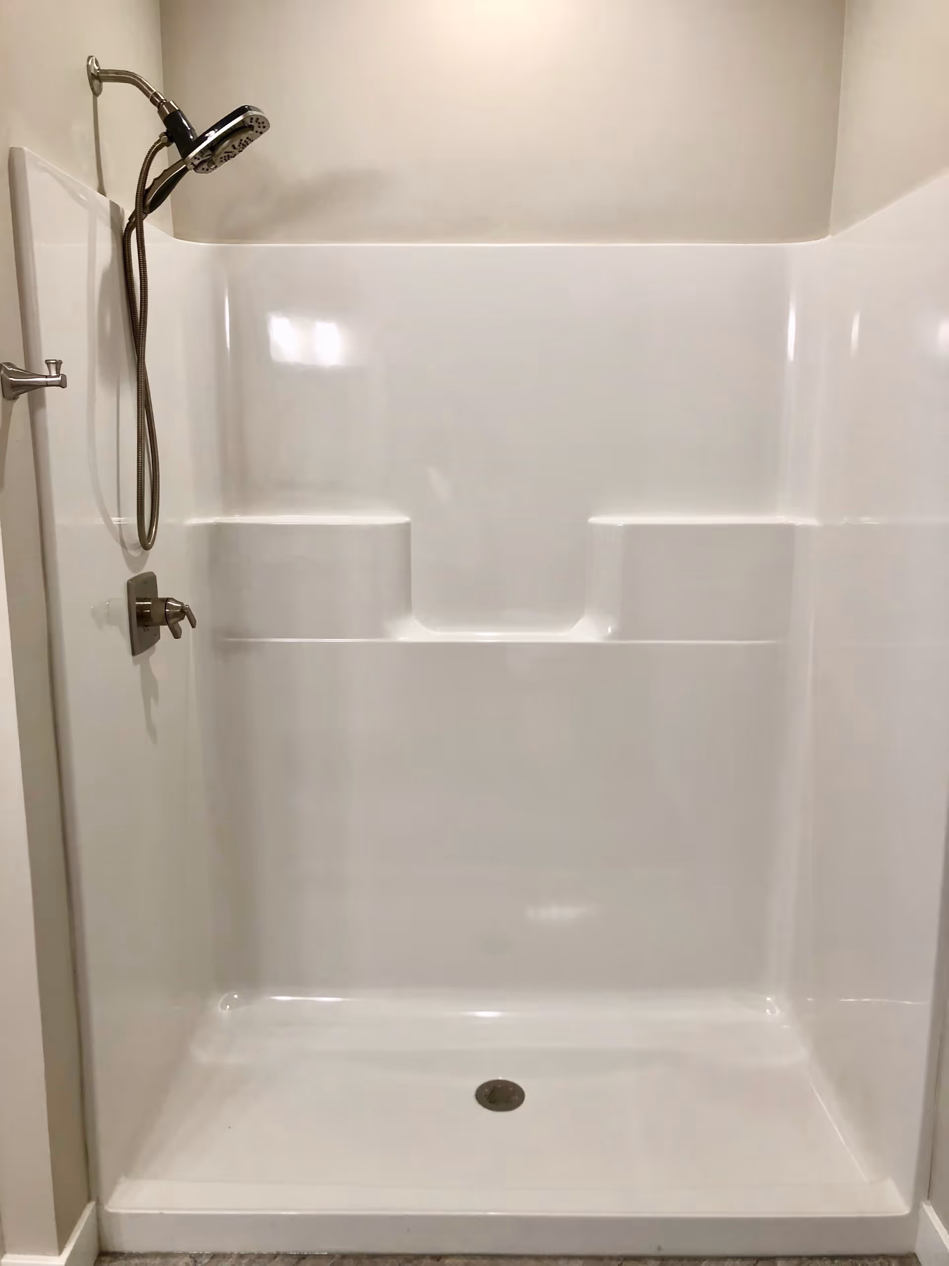 A clean, white shower stall with built-in shelves and a handheld showerhead mounted on the left wall.