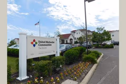 Exterior view of United Methodist Communities at the Shores with a front sign and parked cars.