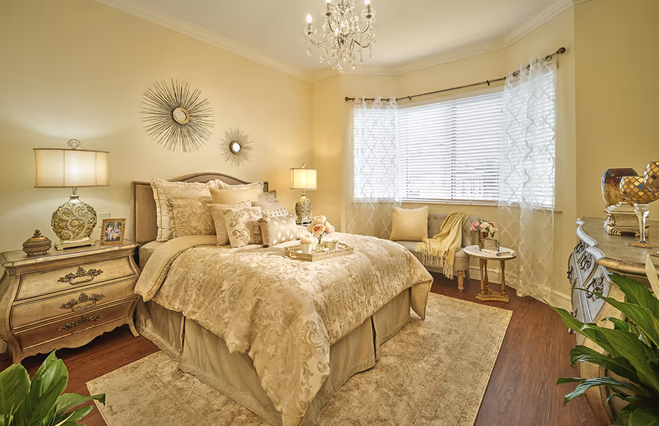 Cozy elegant bedroom with a made bed, nightstands and lamps, chandelier and window seating.