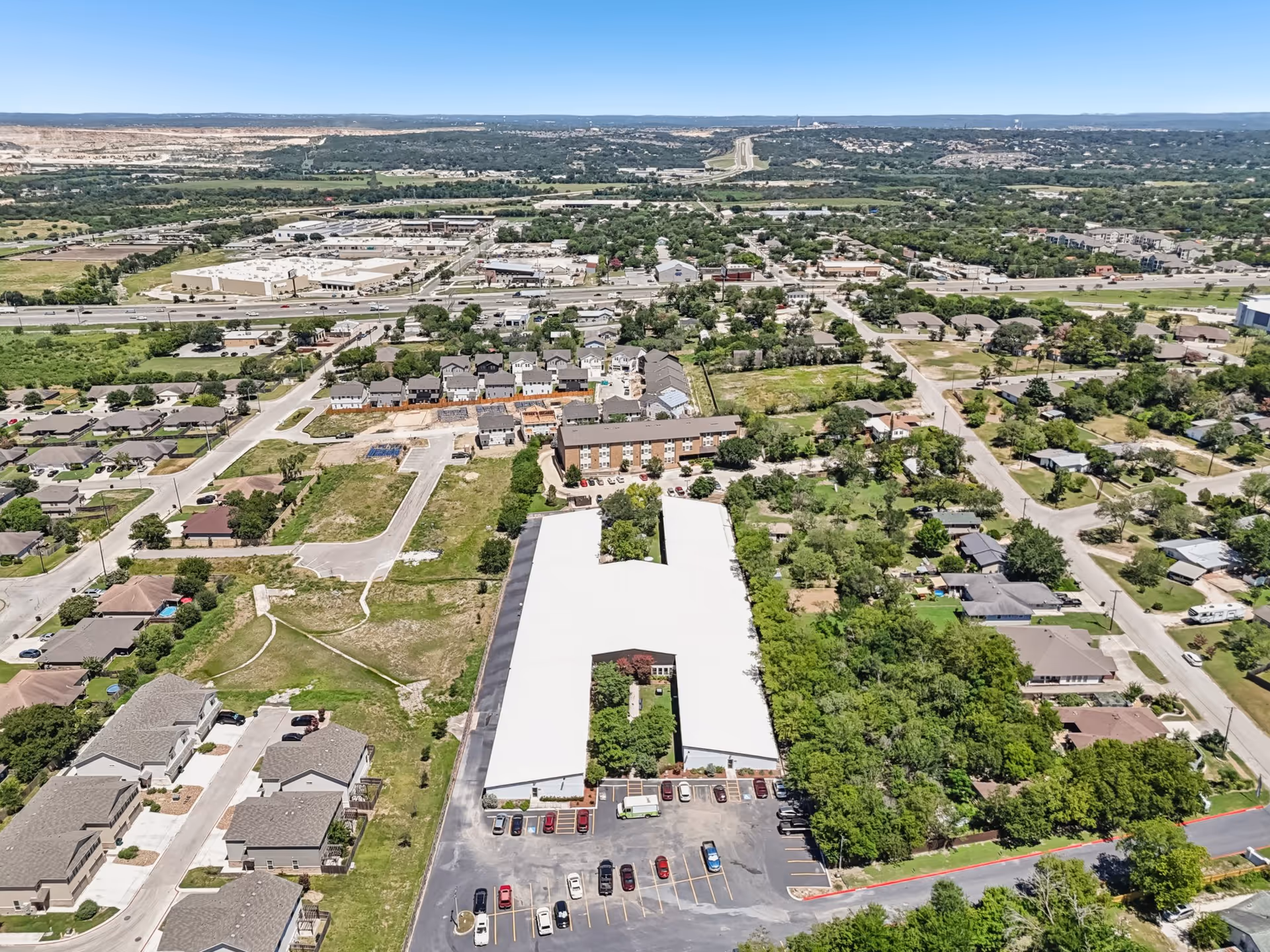Aerial view of a large white-roofed building complex surrounded by roads and trees.