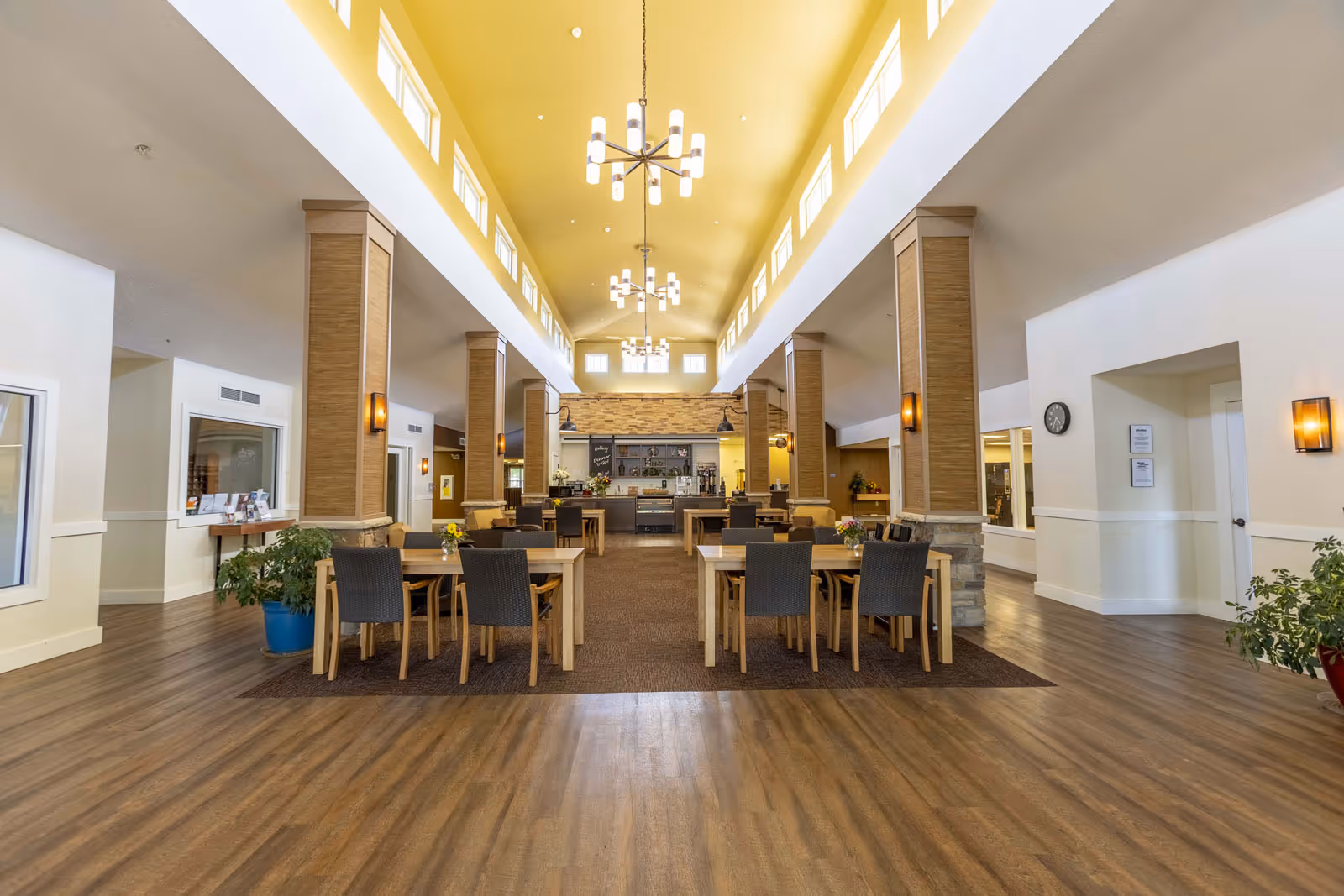 Spacious dining and common area with tables and chairs, high vaulted ceiling with chandeliers, and a serving counter at the far end.