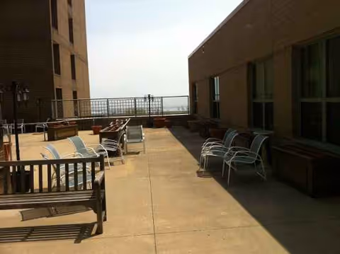 Rooftop patio of a senior facility with benches and metal chairs along a railing.