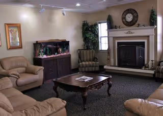 Cozy sitting room with leather sofas, a wooden coffee table, fireplace, wall clock, and a fish tank.