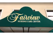 Green awning with the text 'Fairview Nursing Care Center' in yellow script and block letters above an entrance, with part of a beige building and two windows visible.