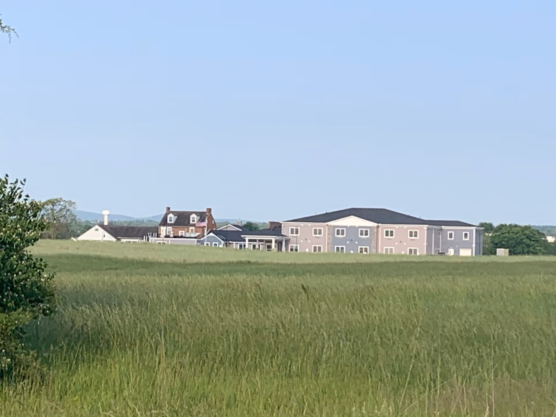 A distant view of Heritage Hills Retirement Home buildings surrounded by a large green field under a clear blue sky.