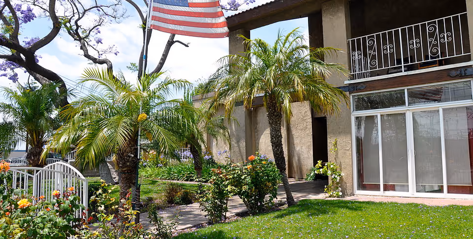 Exterior view of New Horizon Senior Living with palm trees, roses, and an American flag.