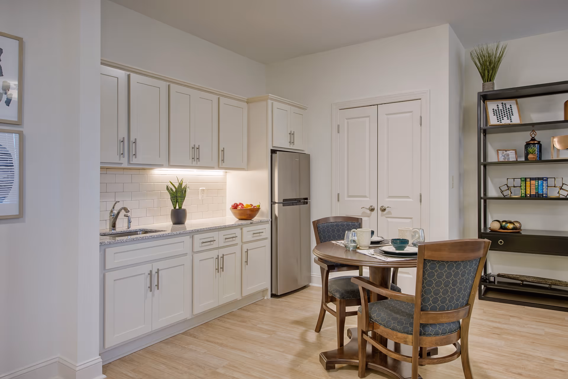 Open kitchen and dining area with white cabinets, a stainless refrigerator, a sink, and a round wooden table with chairs.