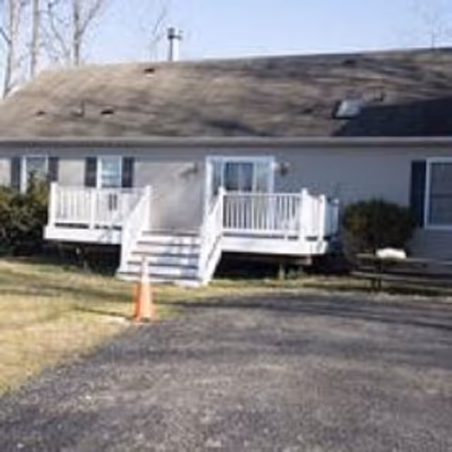 Front of a single-story building with two small white porches and steps, an asphalt driveway and an orange traffic cone.