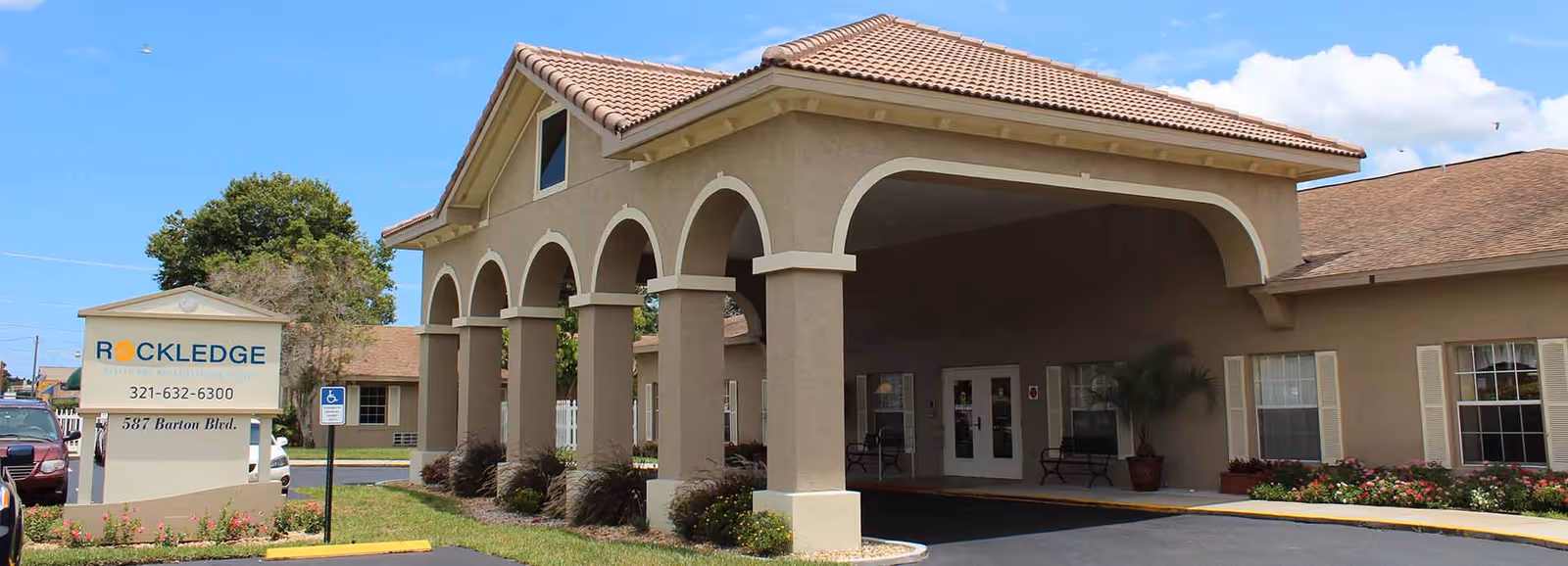 Front entrance of Rockledge Health & Rehabilitation Center showing an arched portico, driveway, and the facility sign on a landscaped lawn.