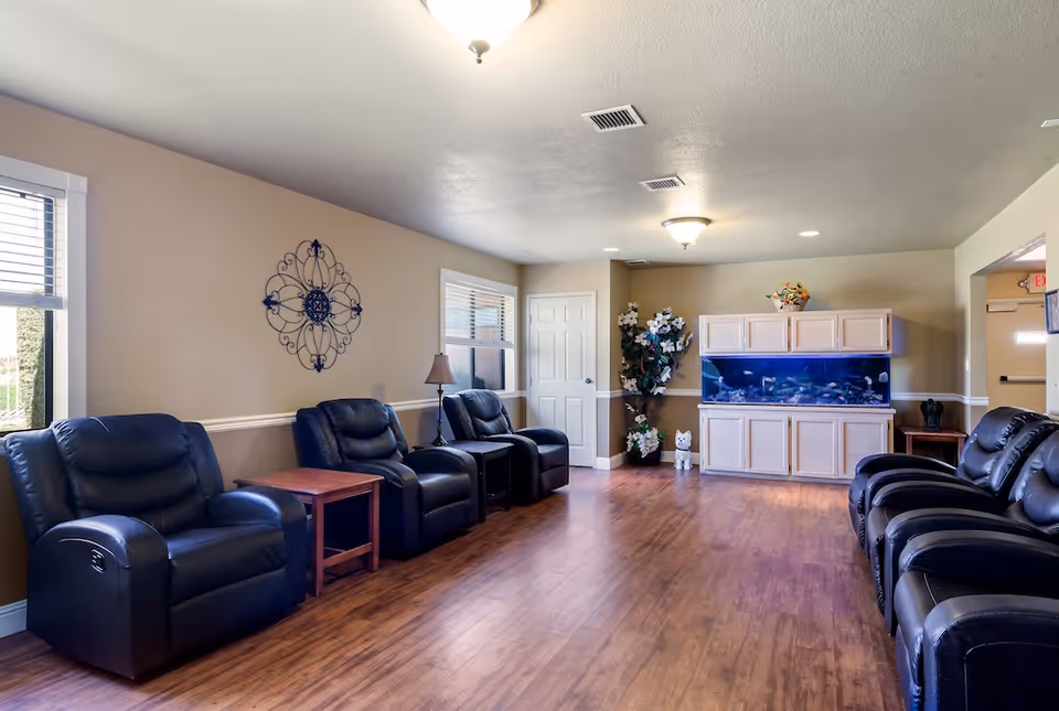 Bright communal seating room with leather recliners along the walls, a large aquarium, hardwood floors, and decorative wall art.