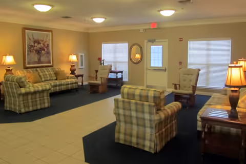 Furnished common living area with plaid sofas and armchairs, side tables and lamps, and an exit door with windows.