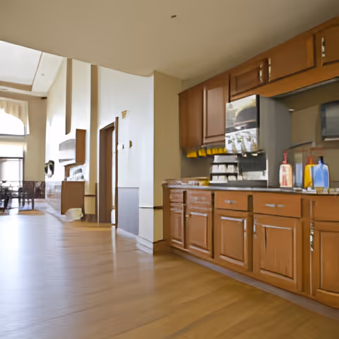 Spacious senior living interior with wooden cabinets and a beverage station on the right and a seating area visible in the distant left.